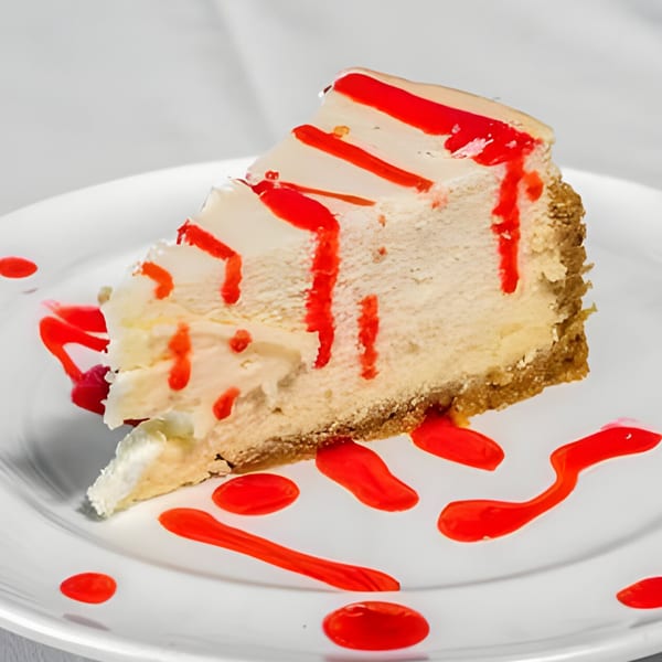 A slice of Carino's cheesecake with a graham cracker crust, drizzled with red raspberry sauce.