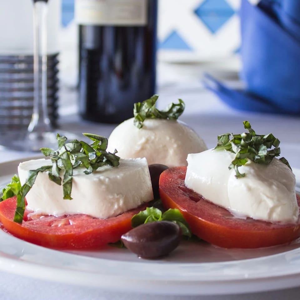 Caprese salad with fresh mozzarella, sliced tomatoes, basil, and olives on a white plate.