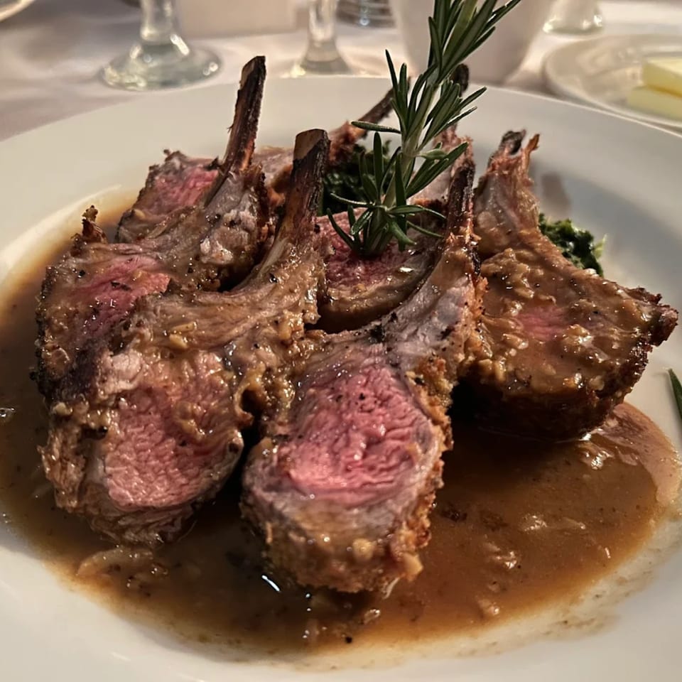 Four lamb chops, medium-rare, with gravy and a rosemary sprig on a white plate.
