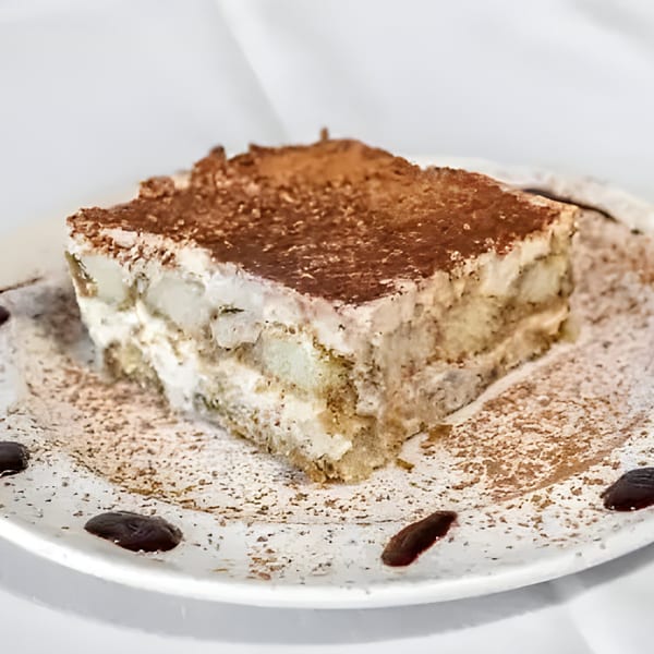 A slice of Carino's tiramisu, dusted with cocoa powder and drizzled with chocolate sauce.