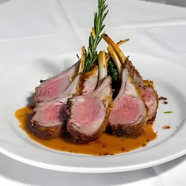 Plated rack of lamb, medium-rare, with rosemary sprigs and a rich brown sauce on a white dish.