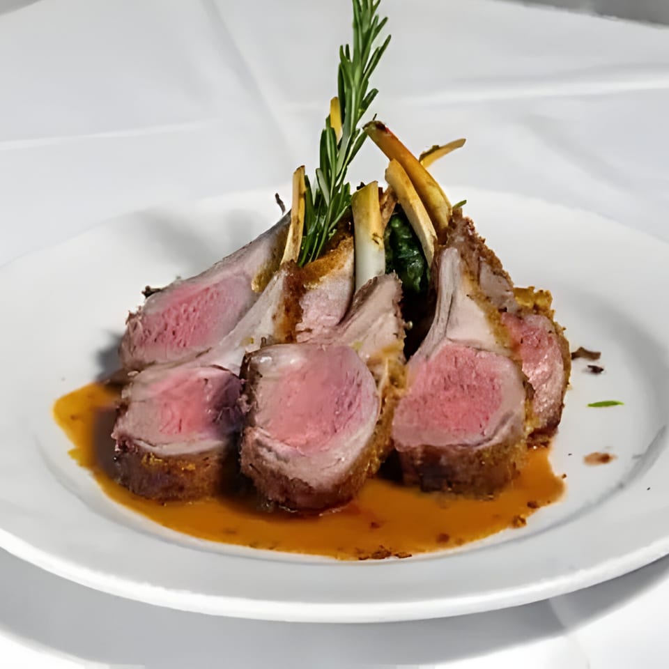 Plated rack of lamb, medium-rare, with rosemary sprigs and a rich brown sauce on a white dish.
