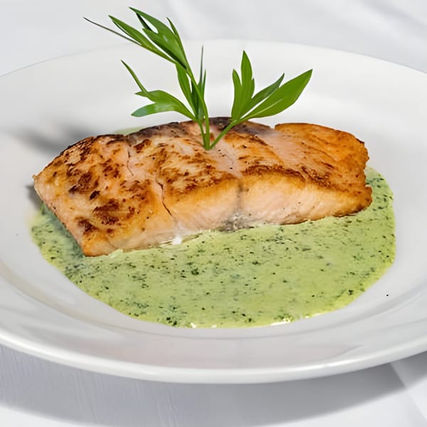 Grilled salmon fillet with a sprig of green herbs, served on a bed of vibrant green sauce.